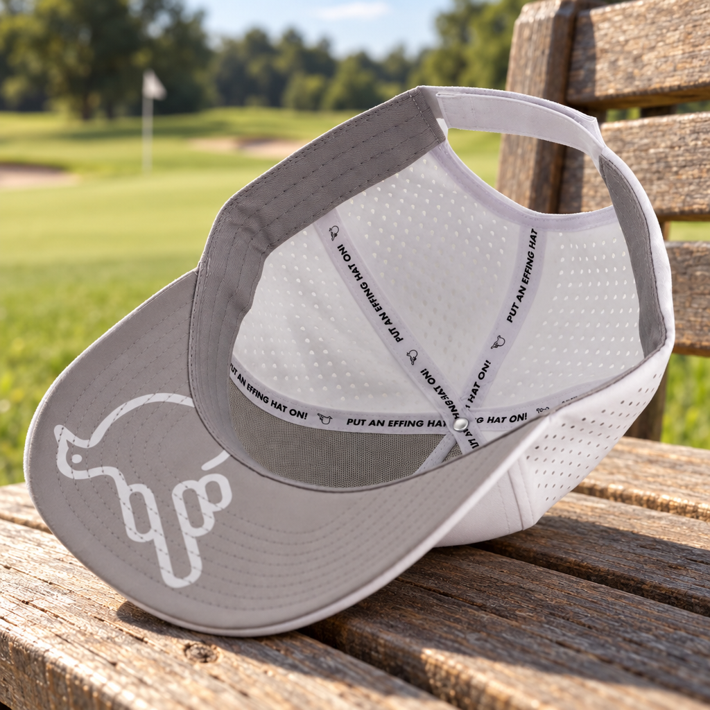 Bye Bye Birdie underside with white Under Bird, gray underbrim and original branded tapes on a timber golf-course bench.