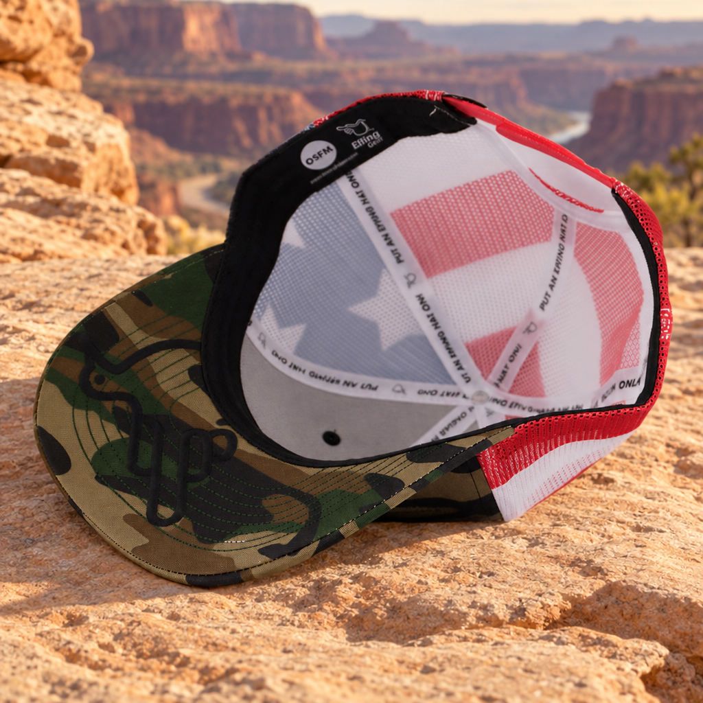 The Camo Stars & Stripes American Bird Trucker underside resting on sandstone, retaining the original camo, tonal black Under Bird, flag mesh and sewn label.