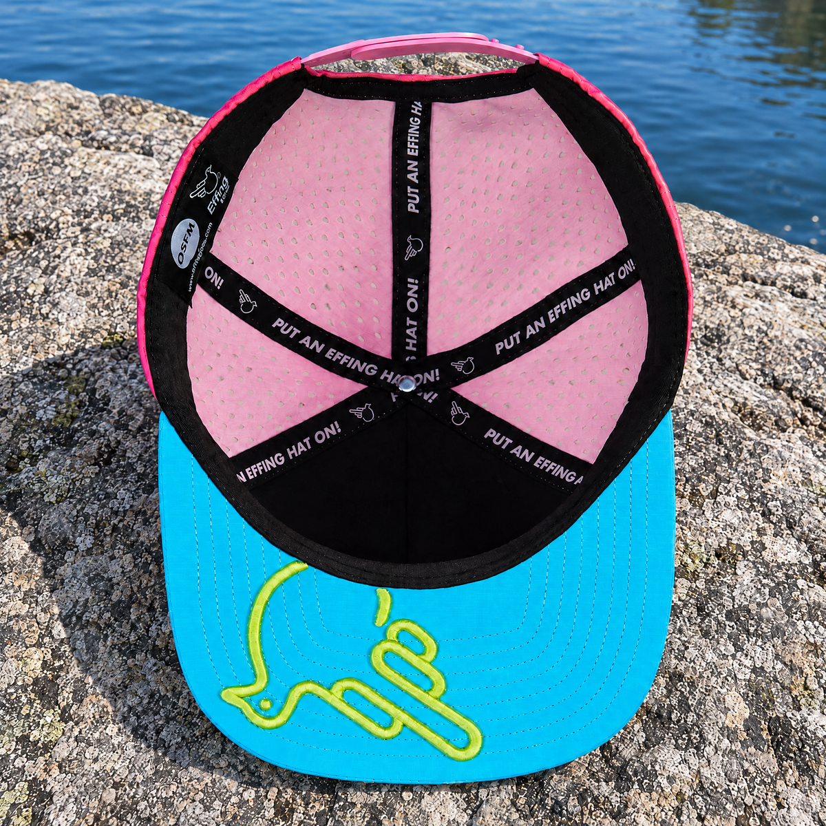 Actual BubbleBird underside in its blue, pink and lime colors, resting on stone by a lake.