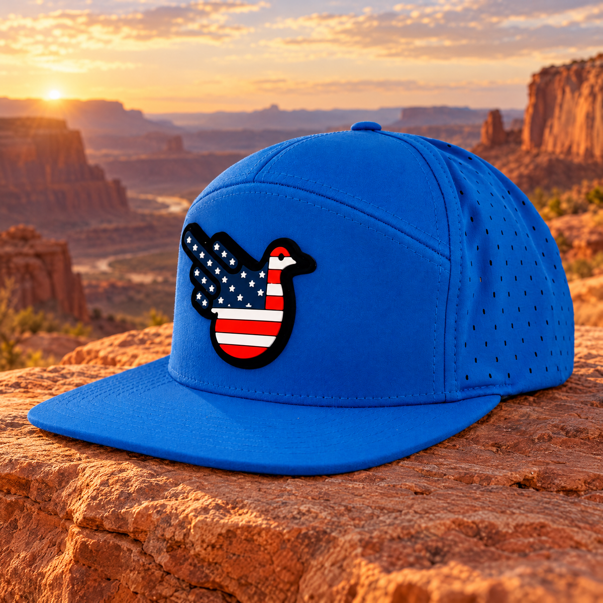 American Cannon Blue flat-brim perforated hat with original molded American flag Bird patch on black backing, supported on sandstone in a generated USA canyon setting.